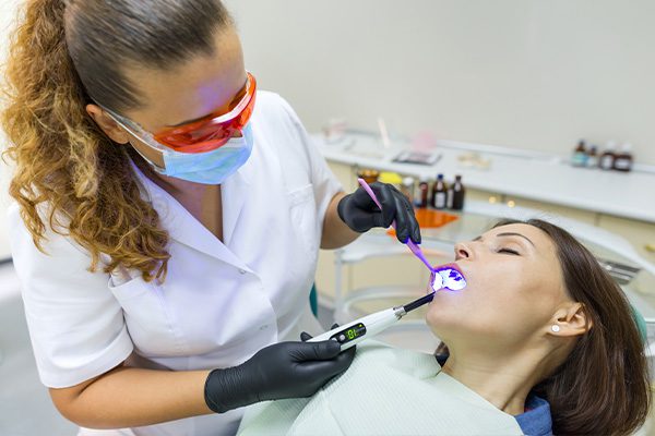 A dentist in Hamilton, Ontario, uses a blue light tool on a sedated patient in a clinical setting.