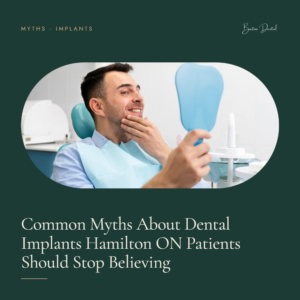 Smiling man checking his teeth with a hand mirror in dental chair - common dental implant myths, Barton Dental Hamilton
