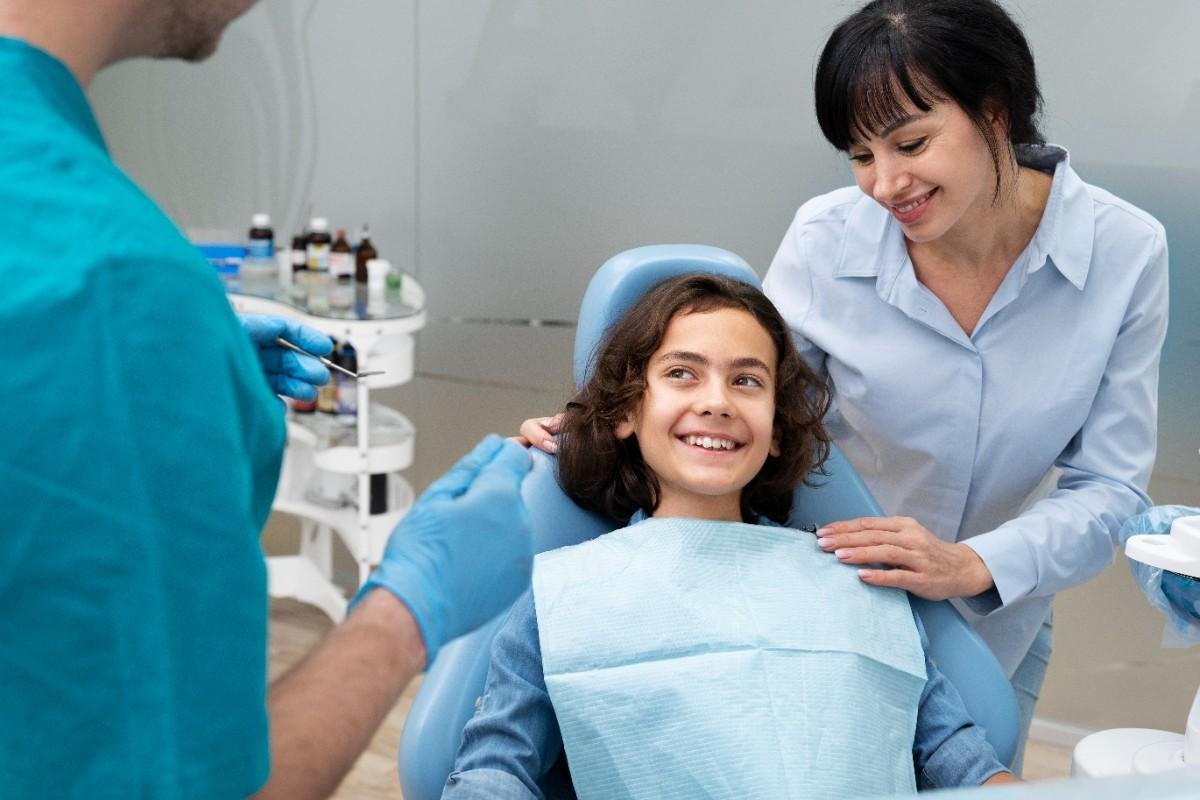 Dentist preparing to examine a smiling child while a parent stands beside the dental chair in a family dental clinic.